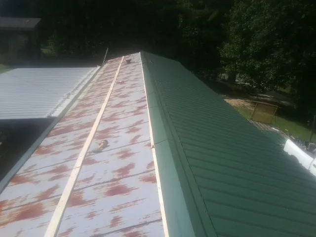 Old rusted panels beside newly installed green metal roofing — Wind Damage Roof Repair by Roofing Brothers in Lena
