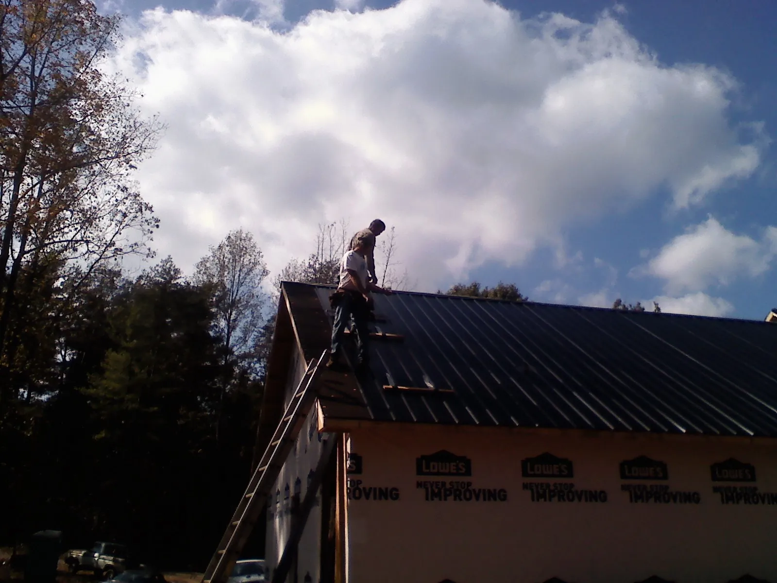Roofer fastening dark metal panels high against a cloudy sky, from a Roof Inspection job in Lena